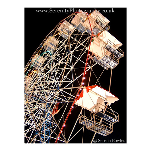 Shot of a big wheel at a fairground, lit up against a night sky.